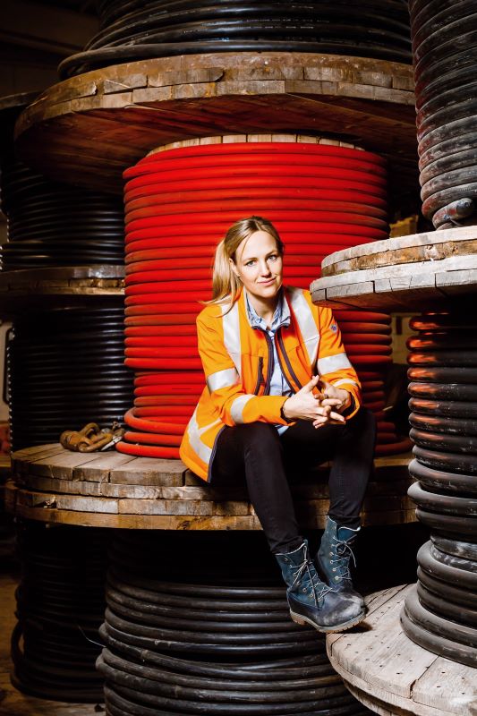 Larissa Zeichardt, Geschäftsführerin von LAT, sitzt in orangener BP® Warnschutzjacke vor einer großen Kabeltrommel.