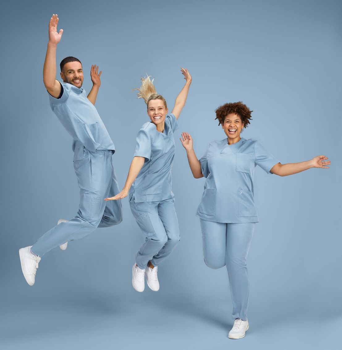 Ein Mann und zwei Frauen in hellblauen, medizinischen Tencel-Outfits springen in die Luft.