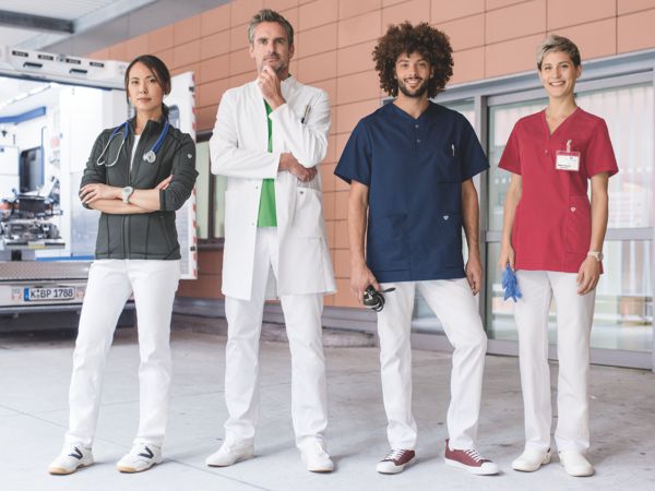 Zwei Frauen und zwei Männer posieren vor einem Krankenhaus in verschiedenen Krankenhausuniformen.