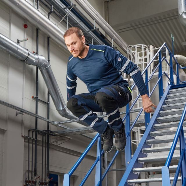 Mann in Multinormkleidung springt Treppe in Inndustriebetrieb heruter.