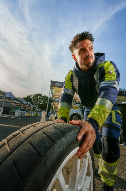 Ein Mann trägt BP® Multi Protect Plus Arbeitskleidung und schiebt einen Autoreifen.