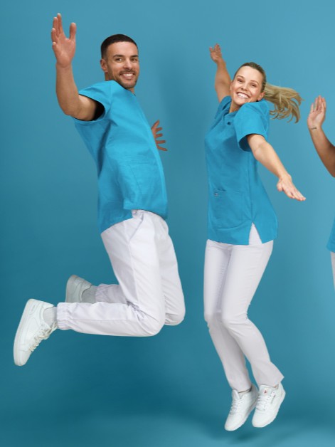 Zwei Pflegerinnen und ein Pfleger in hellblau-weißer Uniform springen vor Freude in die Luft.