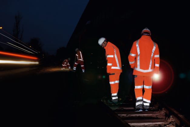 Three men working on a railway track in the dark wearing high-vis protective clothing.