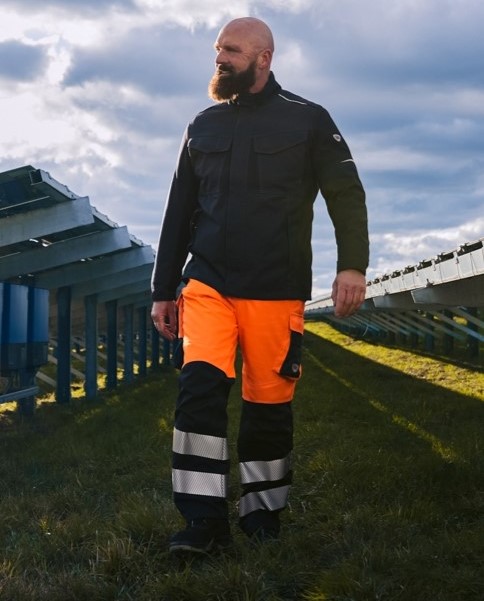 Ein Mann läuft durch eine Photovoltaik Anlage und trägt eine Multinorm Warnschutz Hose.