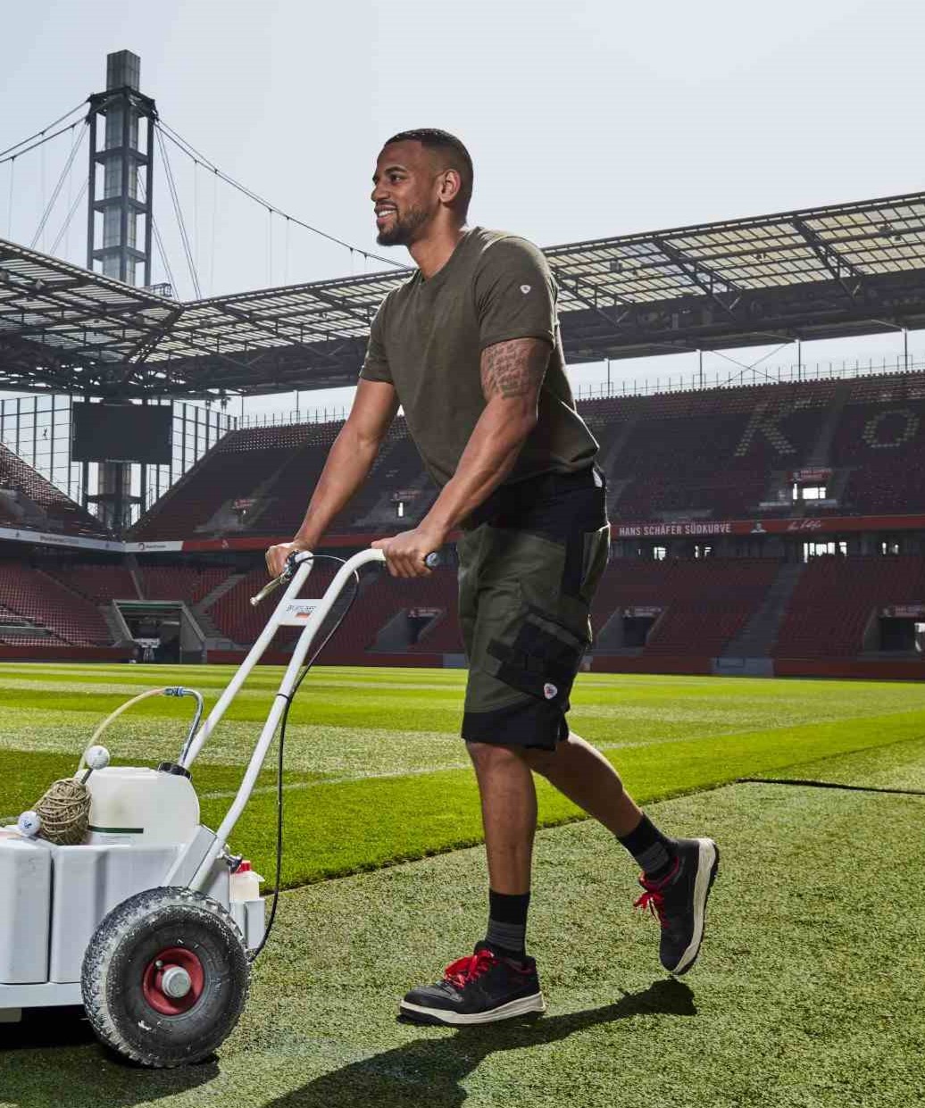 Ein Mann in Arbeitskleidung mäht den Rasen im Rheinenergiestadion.