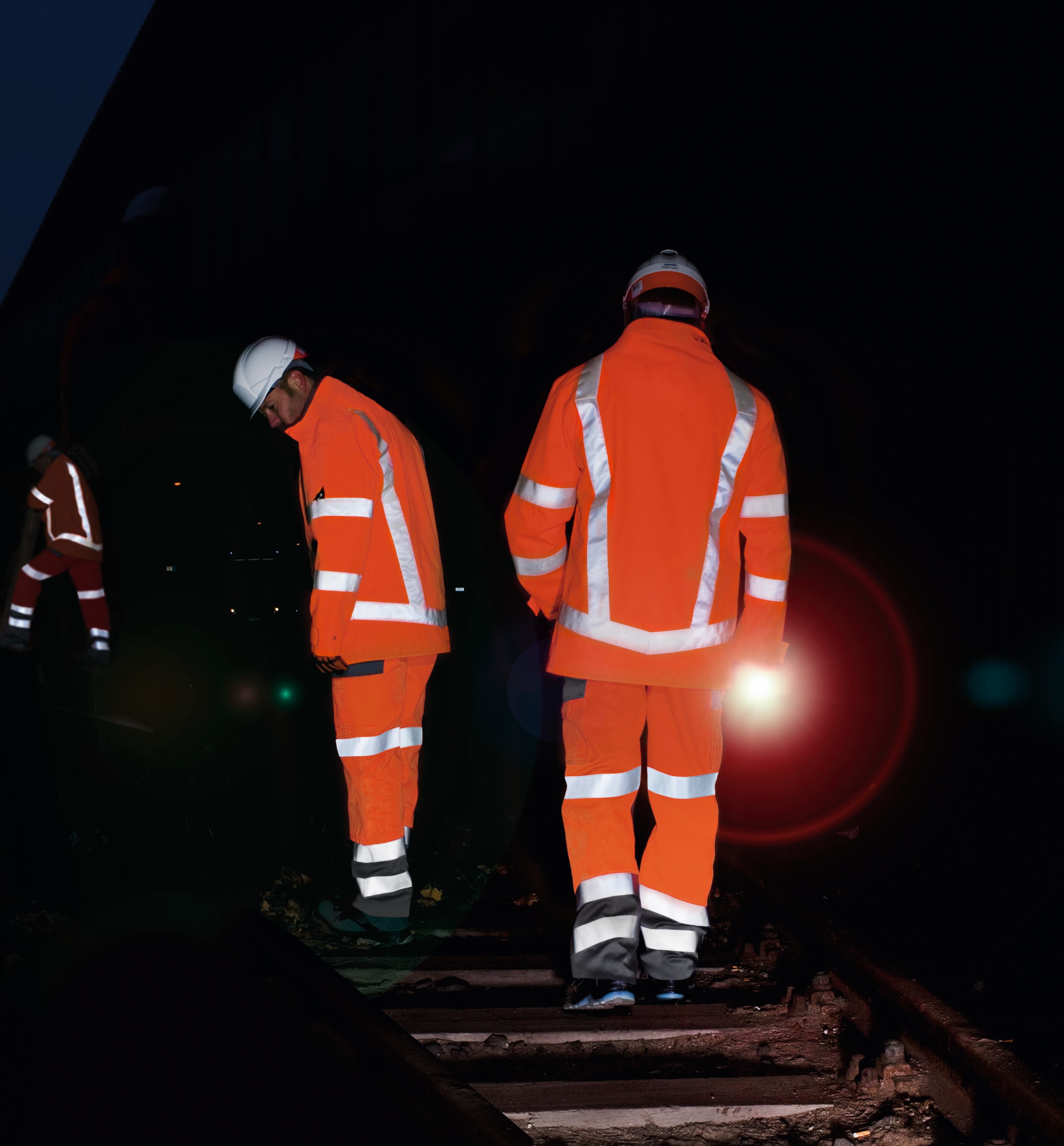 Three men working on a railway track in the dark wearing high-vis protective clothing.