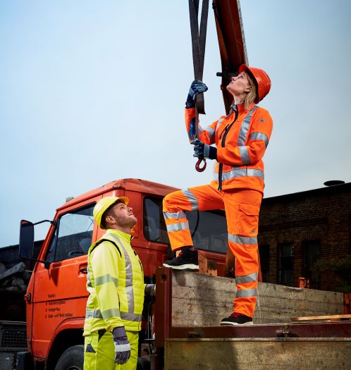 Een vrouw en een man op een bouwplaats dragen gele en oranje opvallende kleding.