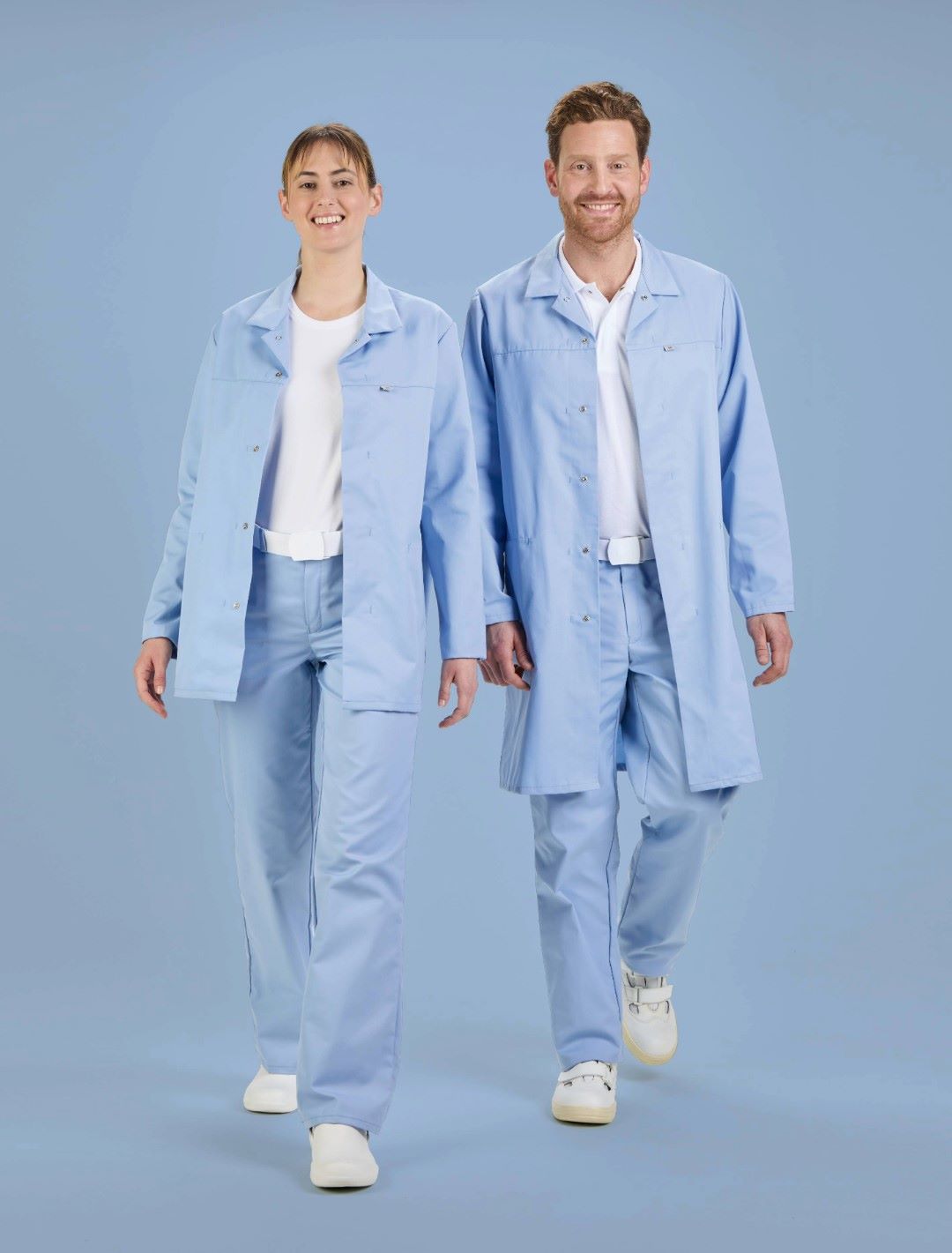 Eine Frau und ein Mann die nebeneinander stehen tragen HACCP Arbeitskleidung in hellblau und lächeln.