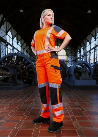 A woman stands in a hall wearing high-visibility orange clothing.