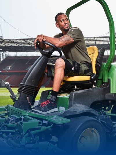 Ein Greenkeeper in Arbeitskleidung mäht den Rasen im Rheinenergiestadion.
