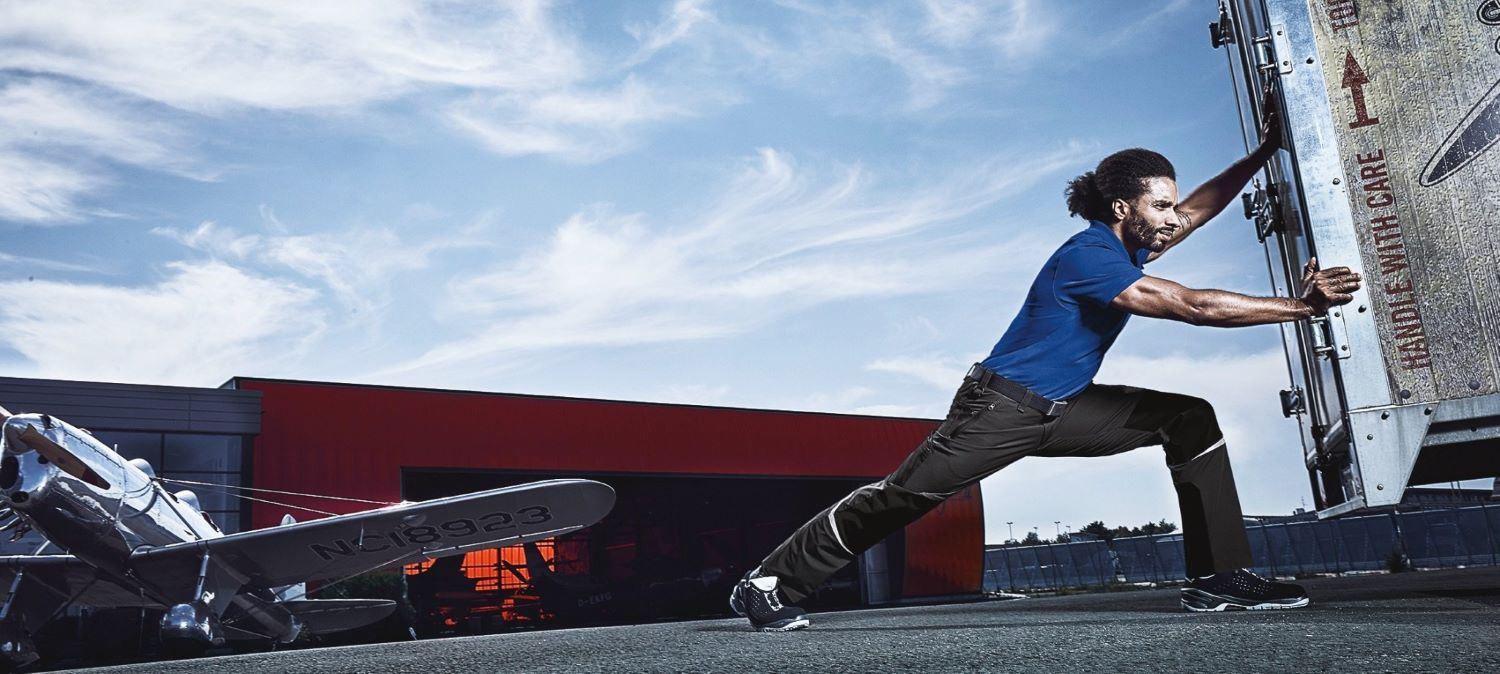 Un technicien événementiel masculin poussant un objet avec un pantalon de travail élastique.