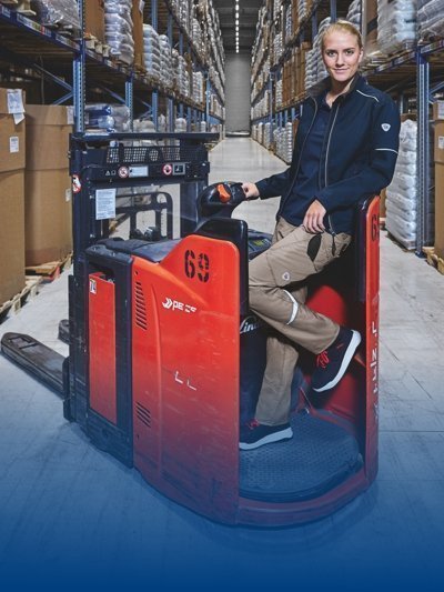 Une employée en tenue de travail se tient sur un chariot élévateur dans un entrepôt.