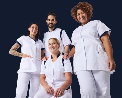 Un infirmier et trois infirmières portent des casaques blanches et des pantalons de travail.