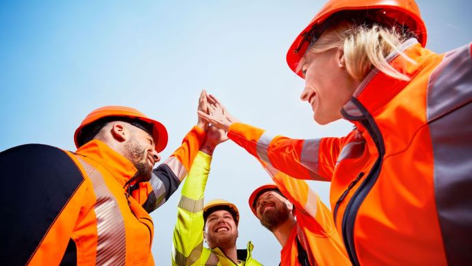 A team in high-visibility clothing give each other a high five in the air.