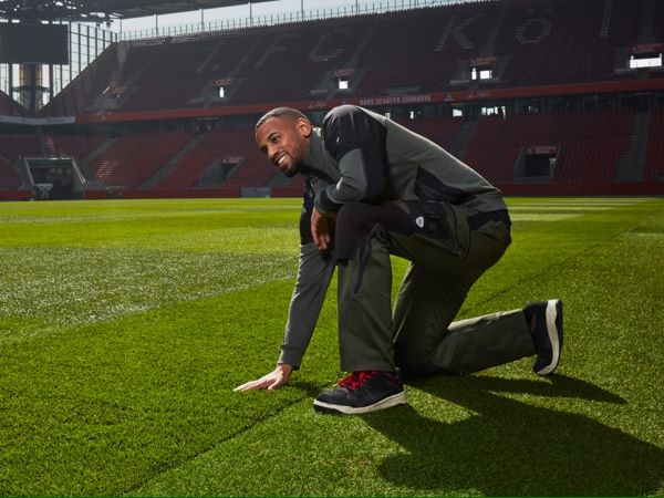 Greenkeeper im Rheinenergiestadion trägt BP® Arbeitskleidung und fasst den Rasen an.