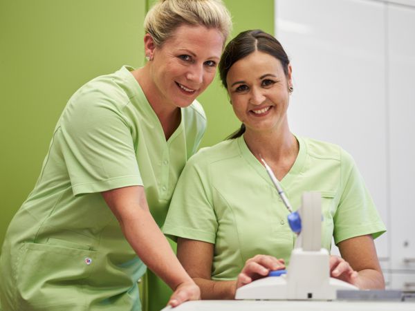 Zwei Frauen posen in einer Klinik mit hellgrünen Kasacks.