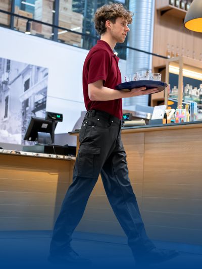 Mann in einem Restaurant trägt eine Servicehose und hält eine Serviceplatte in der Hand.