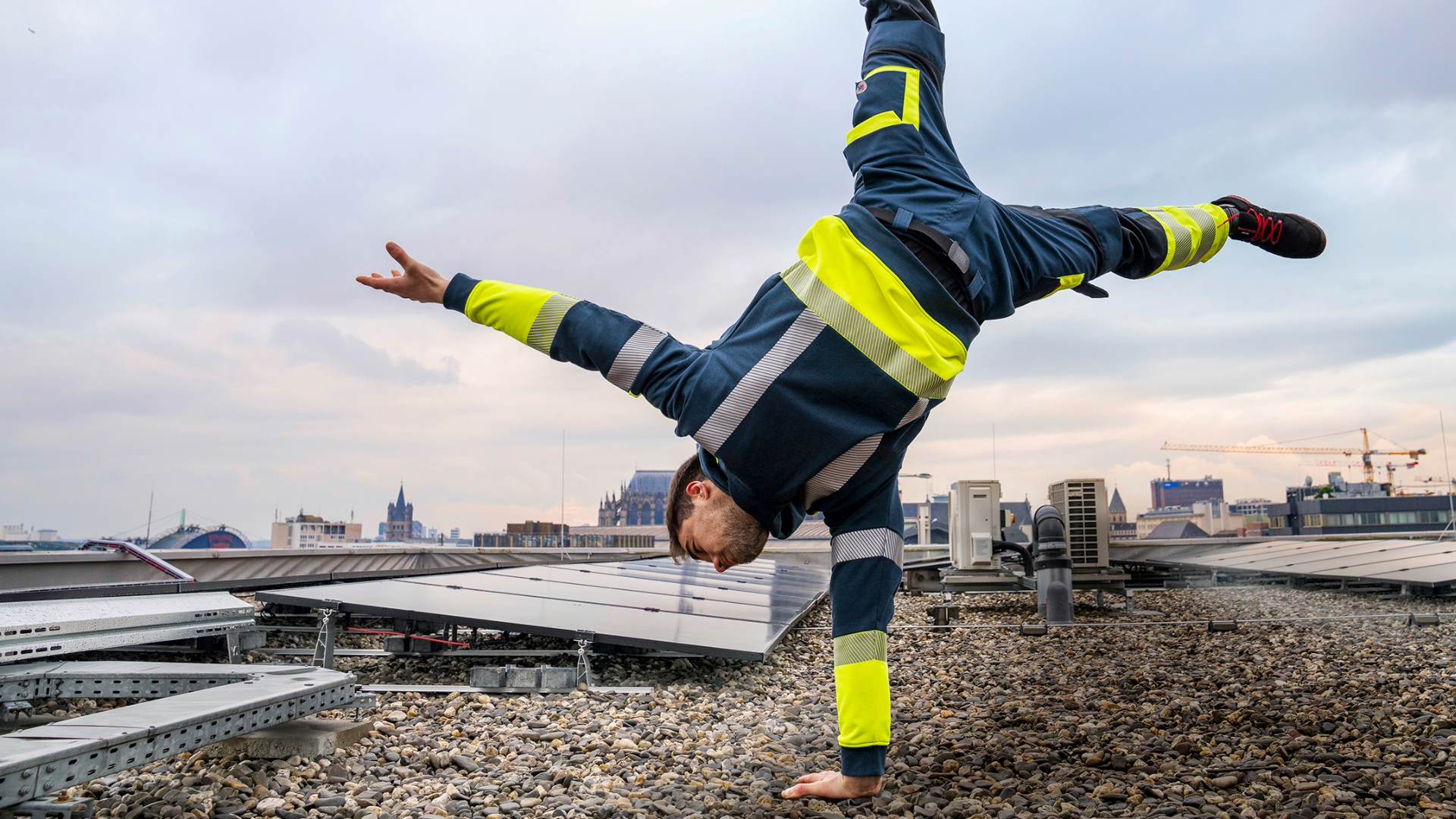 Ein Mann macht einen Handstand auf einem Arm. Er befindet sich auf einem Dach.